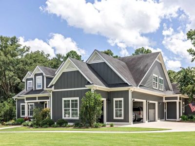 A Large Gray Craftsman New Construction House With A Landscaped Yard And Leading Pathway Sidewalk